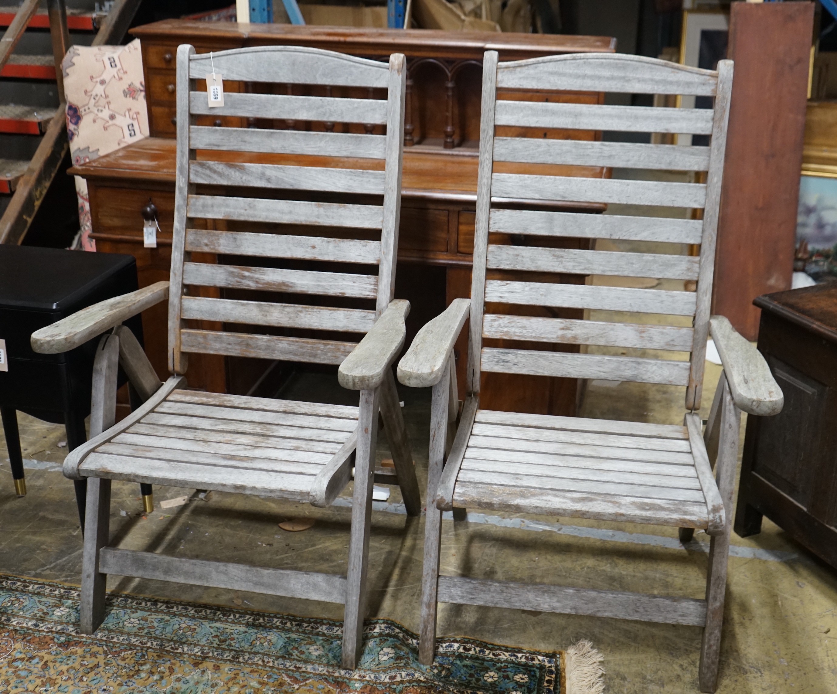 A pair of weathered teak folding garden armchairs, height 112cm